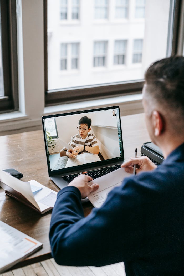 Professional participating in an online video conference with a colleague at a wooden desk.