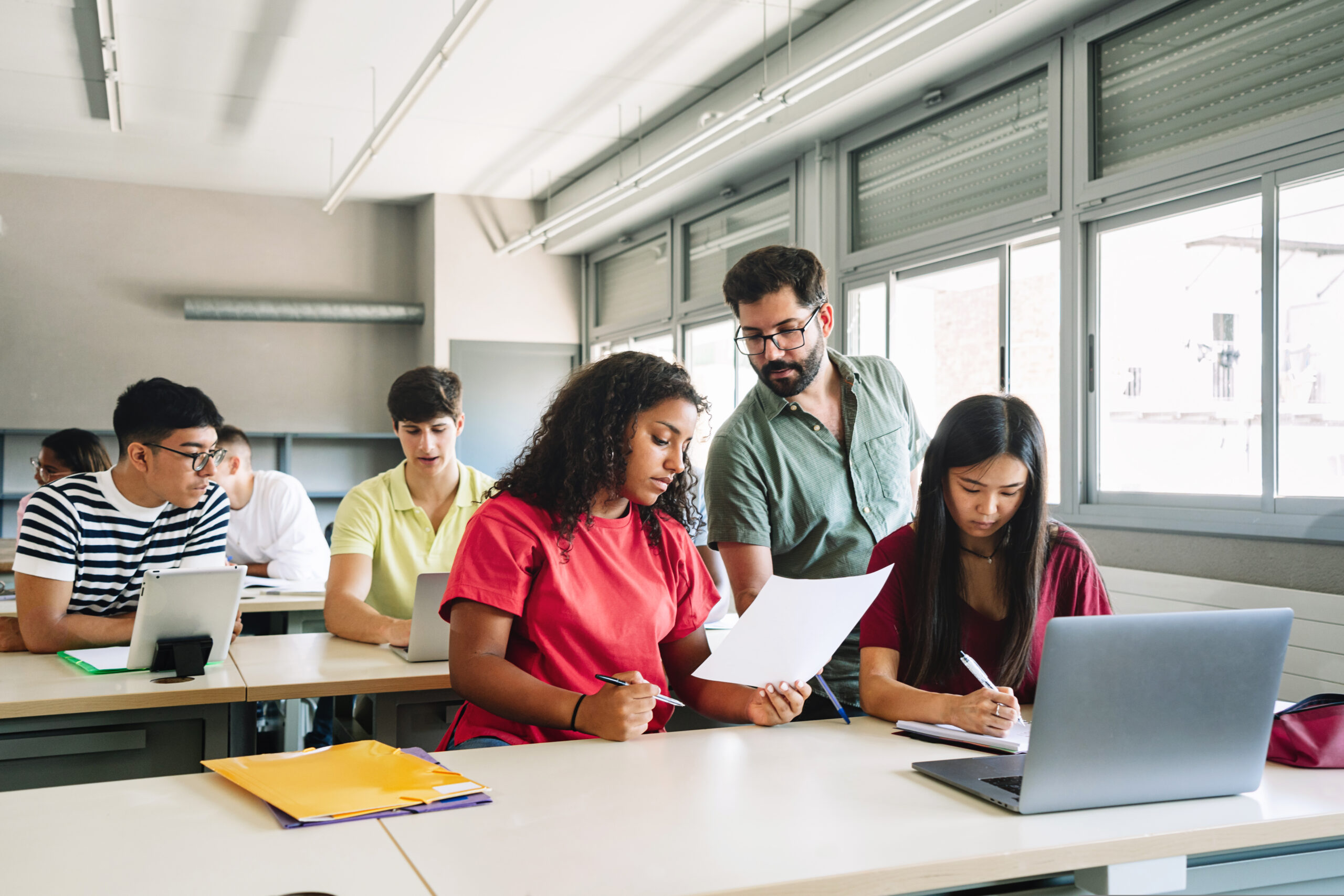 friendly professor explaining exercise to students in high school classroom. young teacher with beard helping teenager girl focus on male teacher