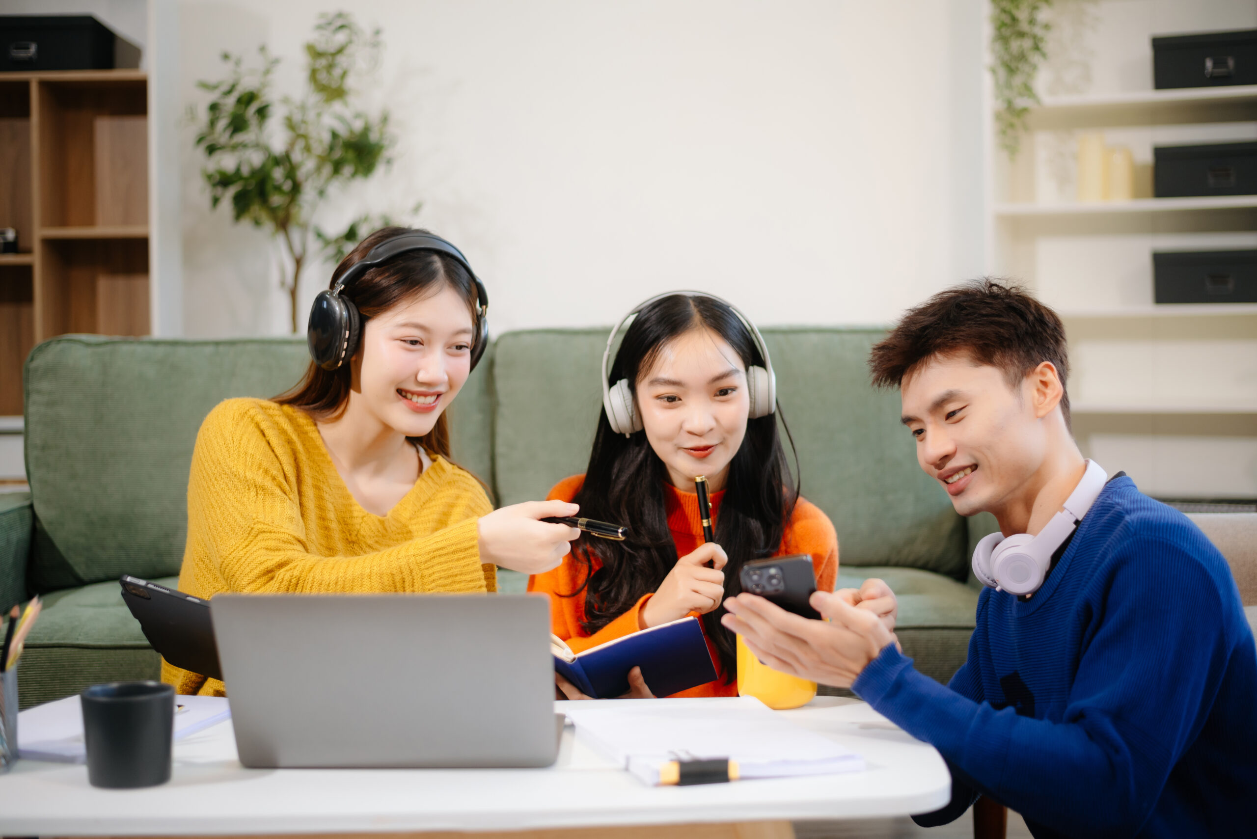 group of young asian students working on a project with laptops and tablets. cozy indoor setting,