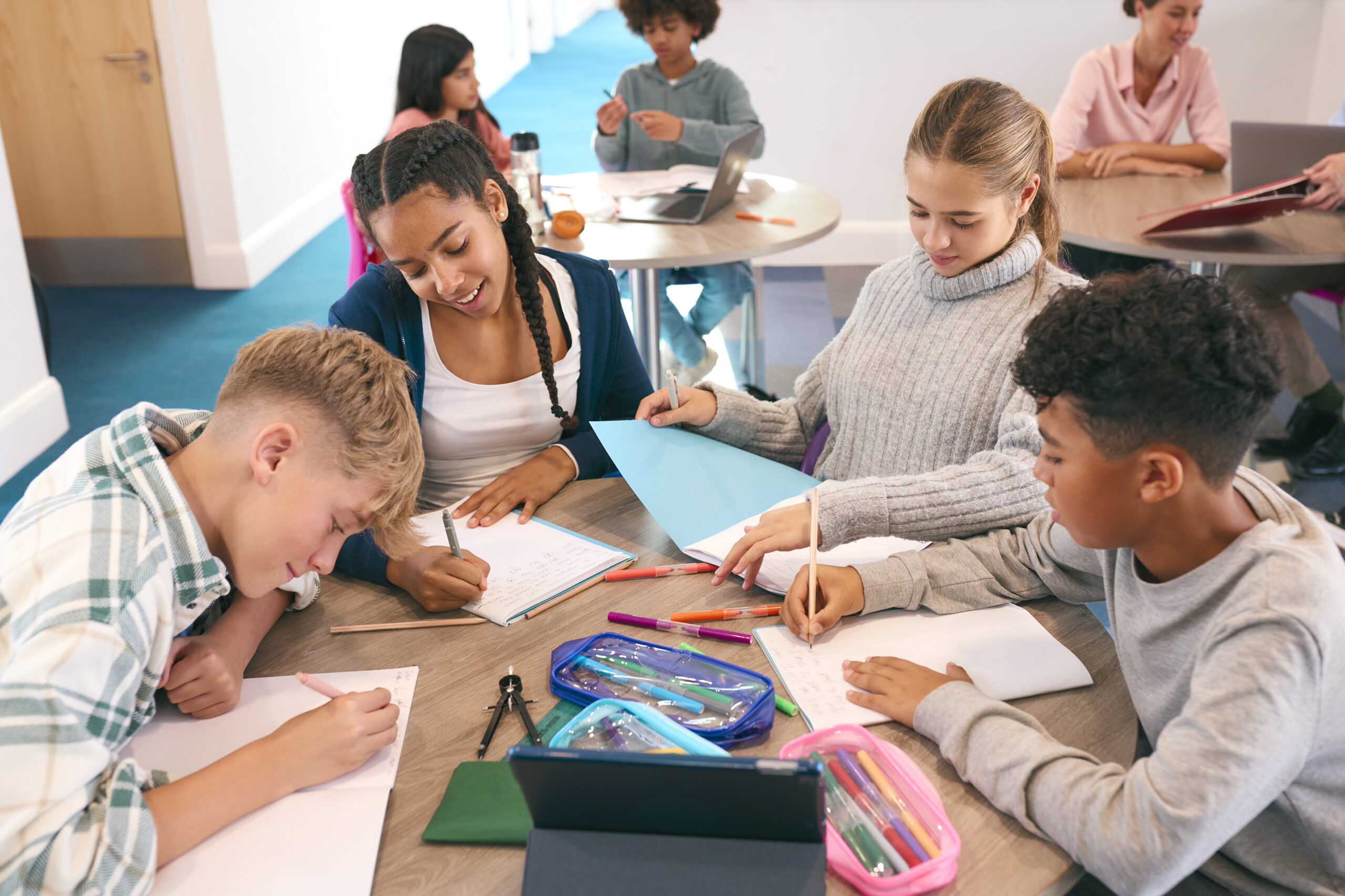 secondary or high school students collaborating in study area with teachers in background
