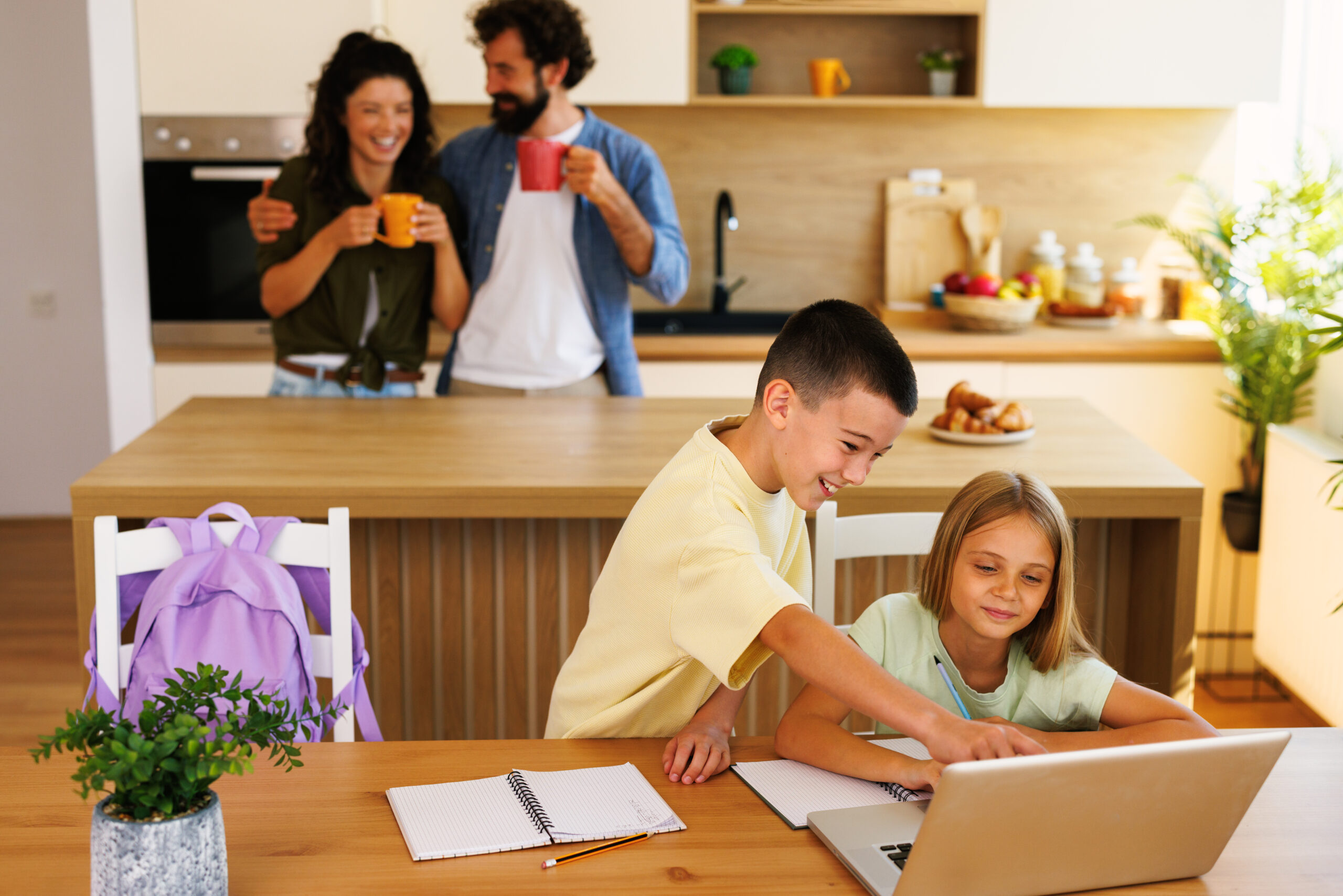 brother and sister using laptop for homework while parents enjoy coffee in the background, promoting family and education