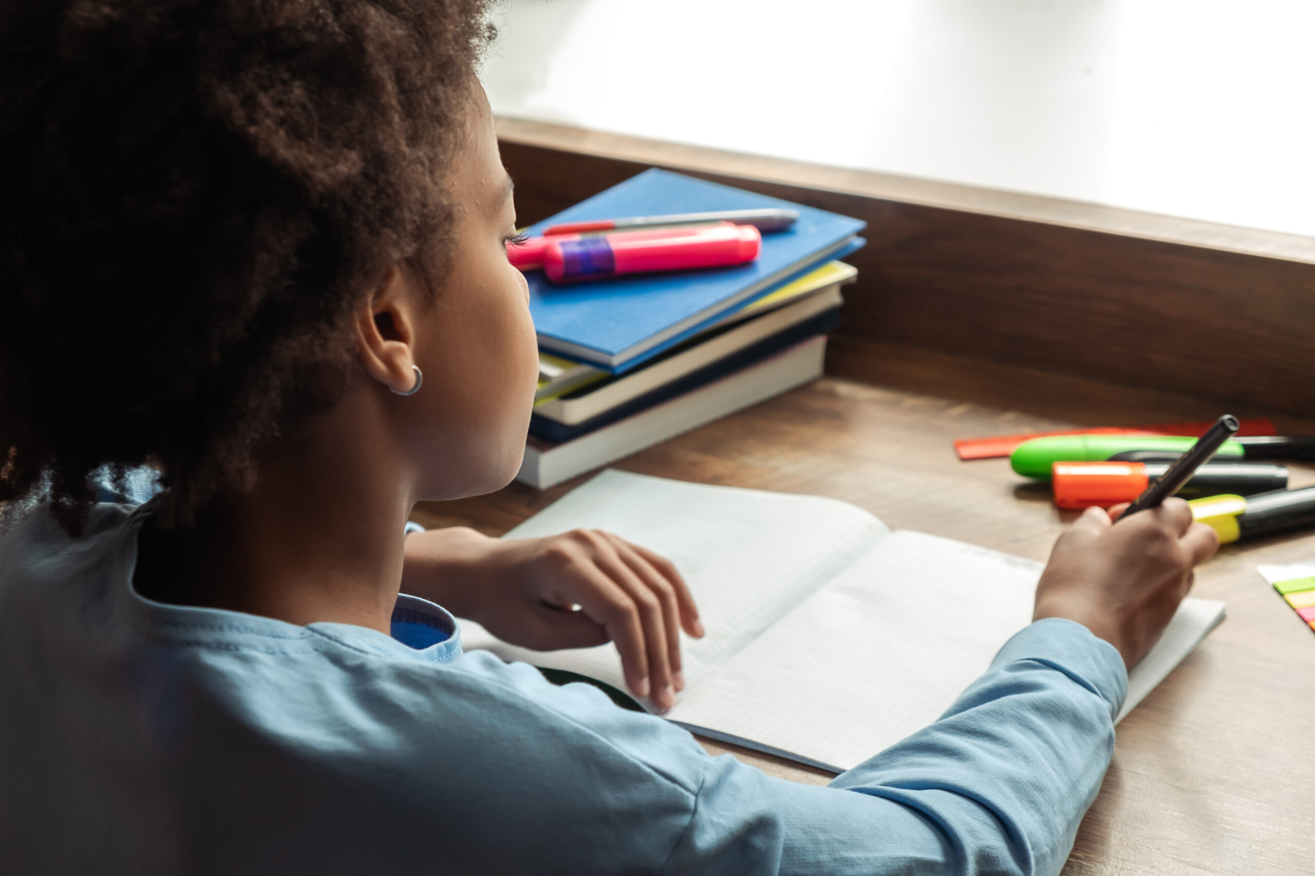 african american preteen girl doing homework,making notes in notebook at home at her desk.close up, rear view.back to school concept.school distance education,home schooling,diverse people