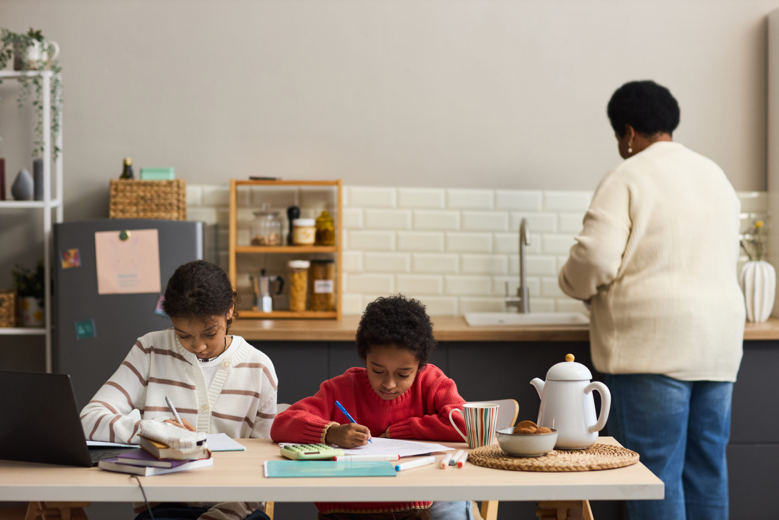 black woman preparing food while two children studying at kitchen table