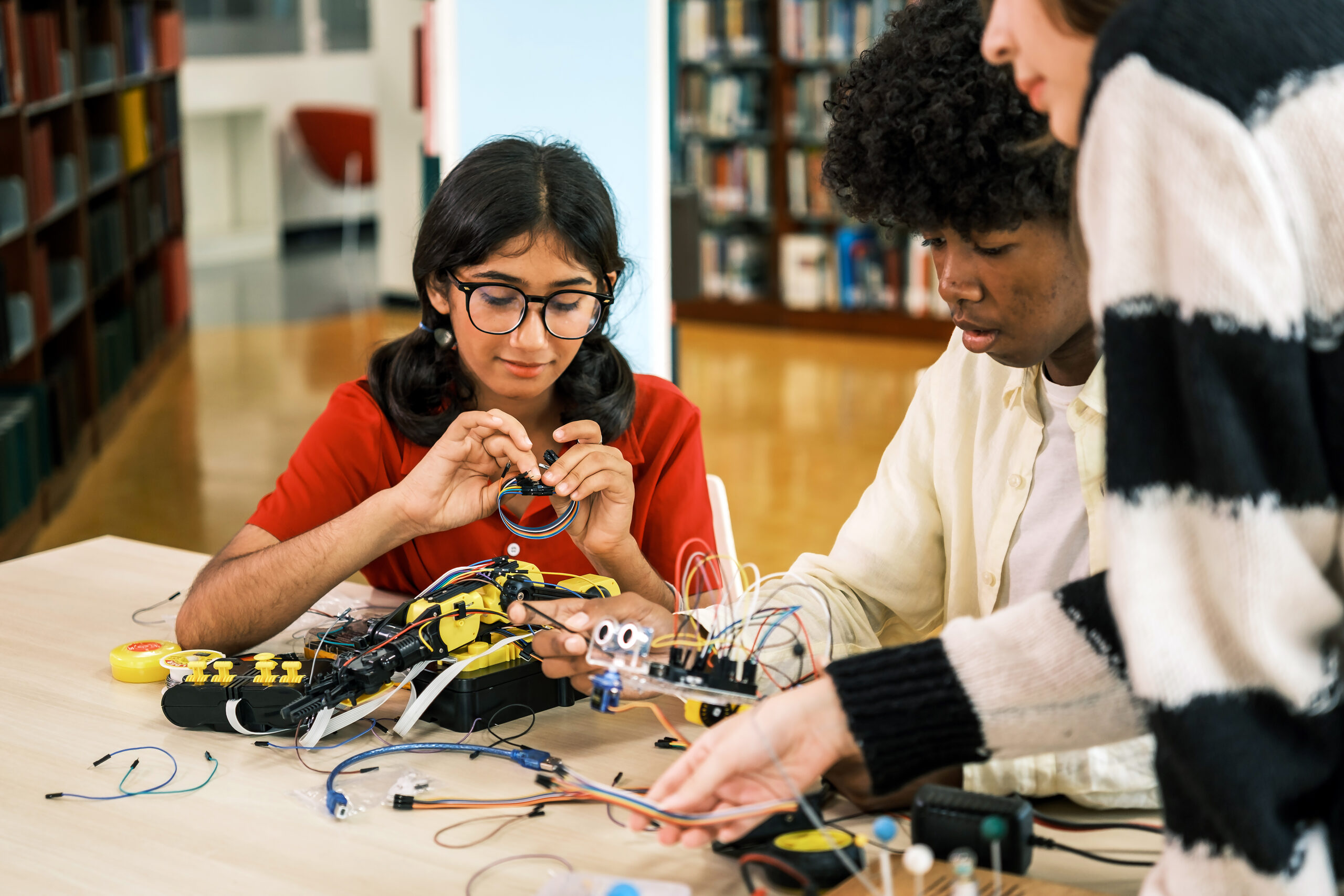 an indian girl and african boy work together on a robotics project using electronic components in a classroom or library setting, highlighting collaboration, stem learning, and academic curiosity.