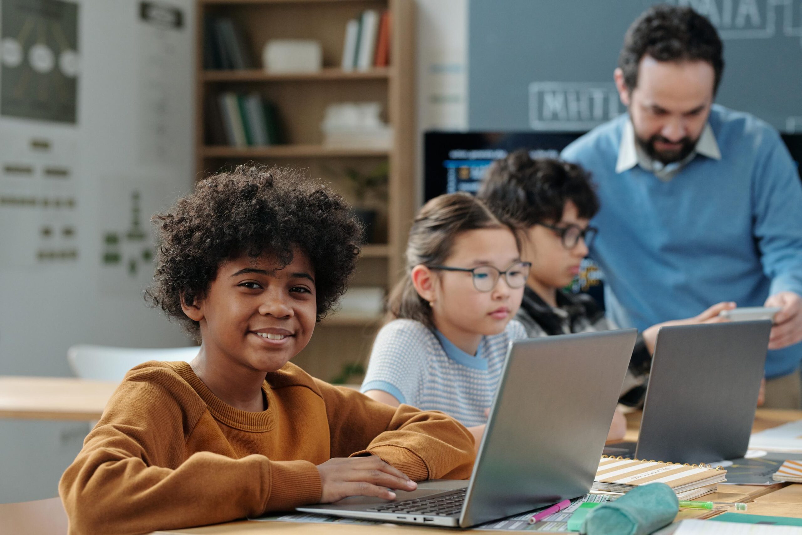 children studying using laptops with teacher assisting