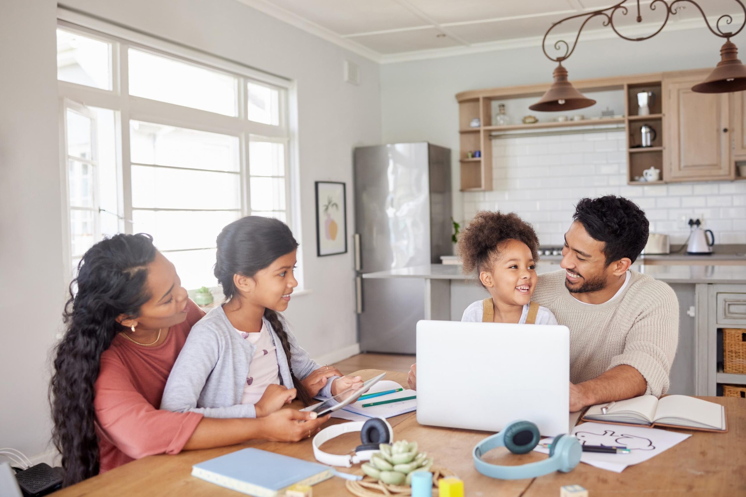 How to Choose a Flexible, Accredited K-12 Virtual School That Fits Your Family’s Routine in 2026 mixed race family using information technology at home. two little girls doing homework in the kitchen with help from their mother and father. parents and children working on school work together